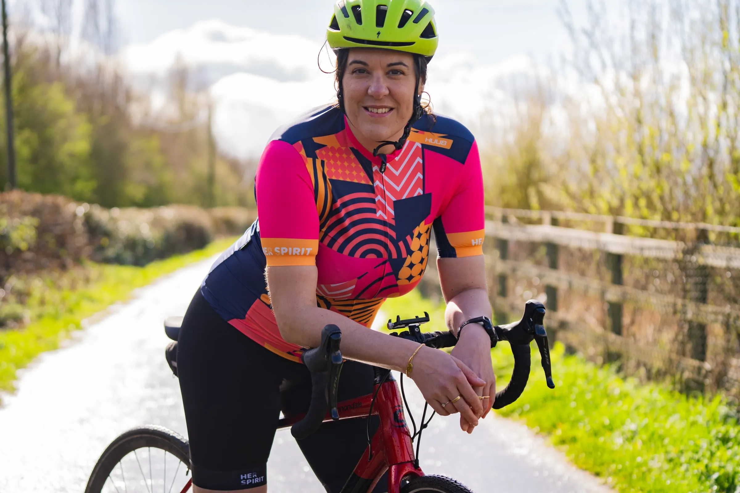 A cyclist leaning on her handlebars on a country lane, wearing a HUUB Her Spirit jersey and bib shorts